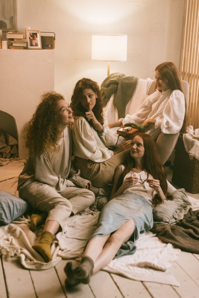 Four women enjoying a cozy indoor sleepover with warm lighting and friendly conversation.
