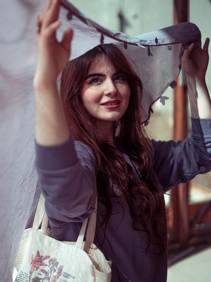 Charming young woman smiles while holding fabric above her head outdoors in Baghdad.
